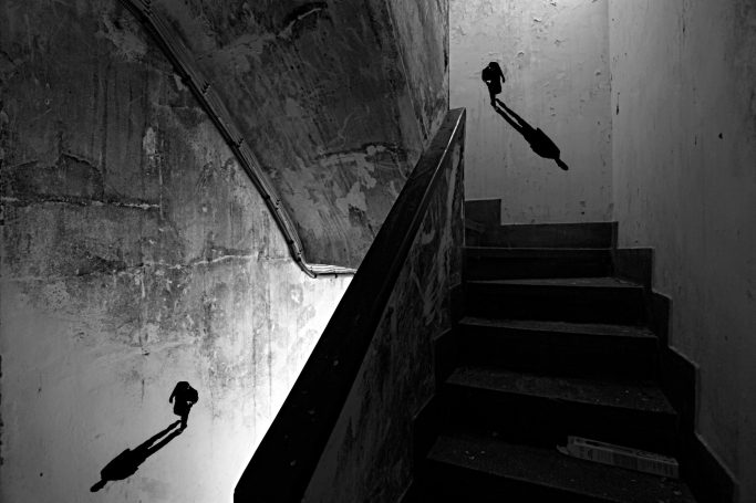 Fotografía de escalera en claroscuro con sombras alargadas proyectadas en la pared. 